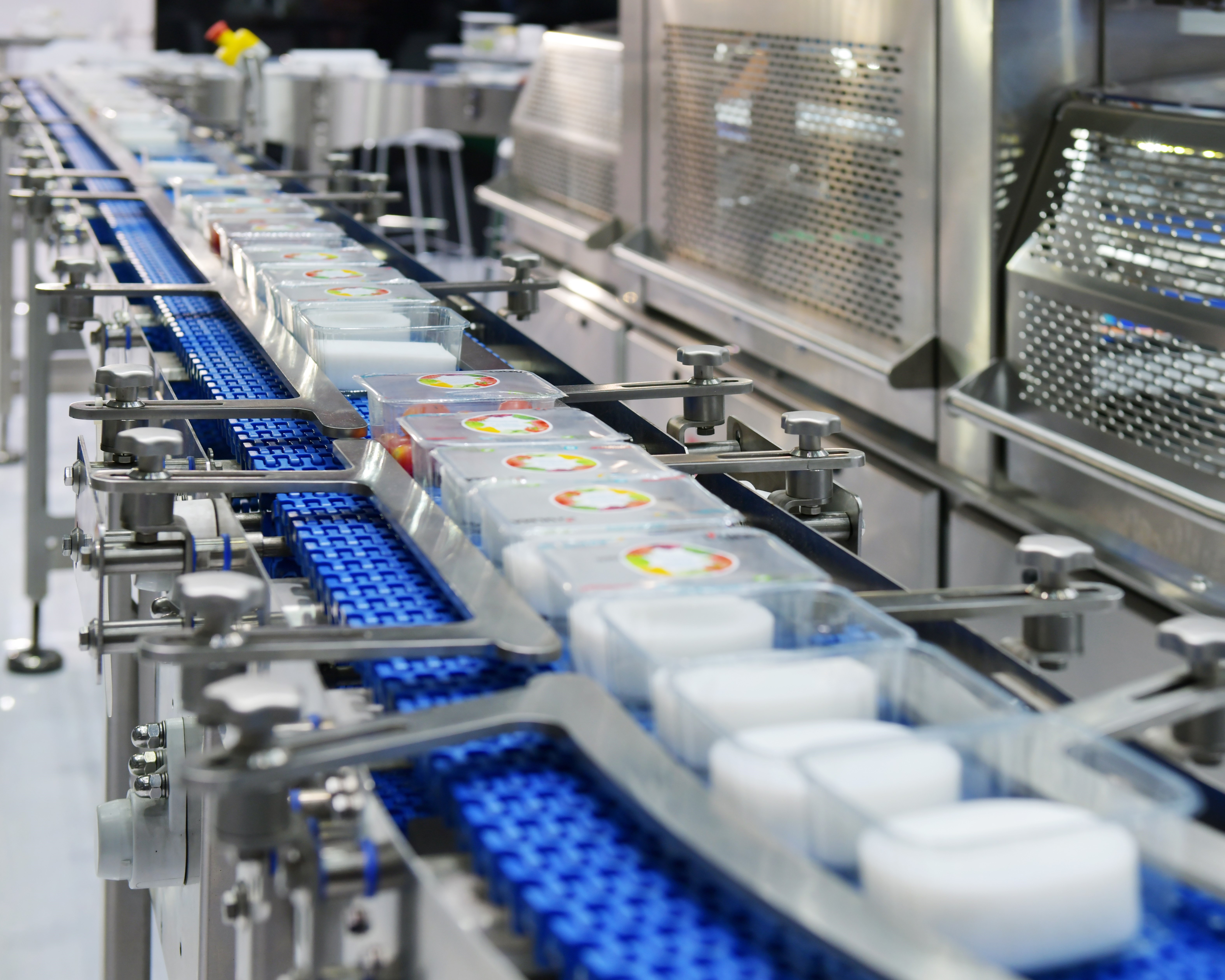 Plastic tubs being transported down a conveyor belt with machinery putting a lid on every tub.