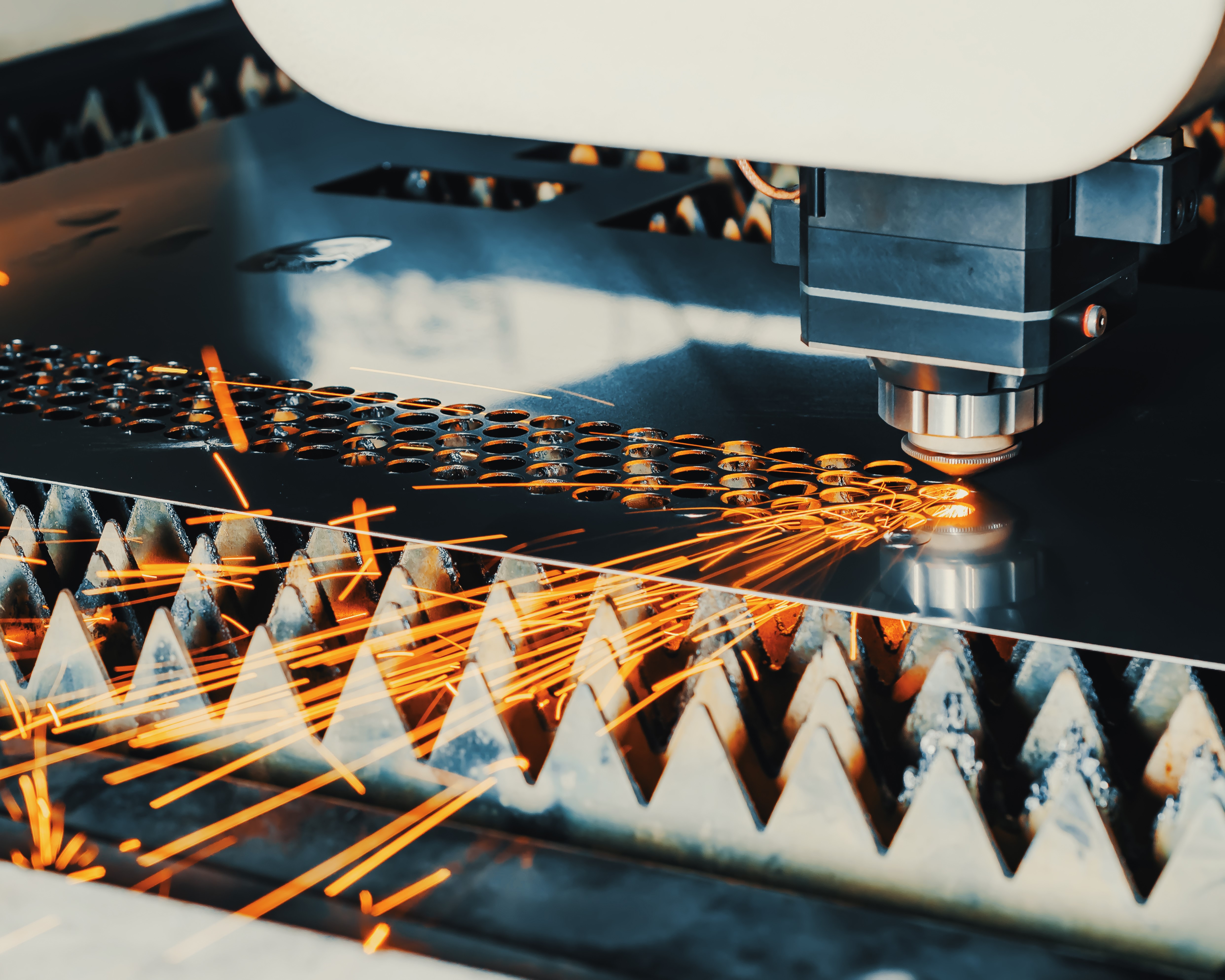 A laser cutter operating on a metal sheet engraving circular holes.
