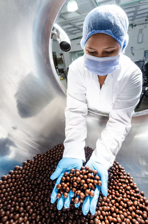 A woman with a hair net and face mask with a handfull of chocolate balls.